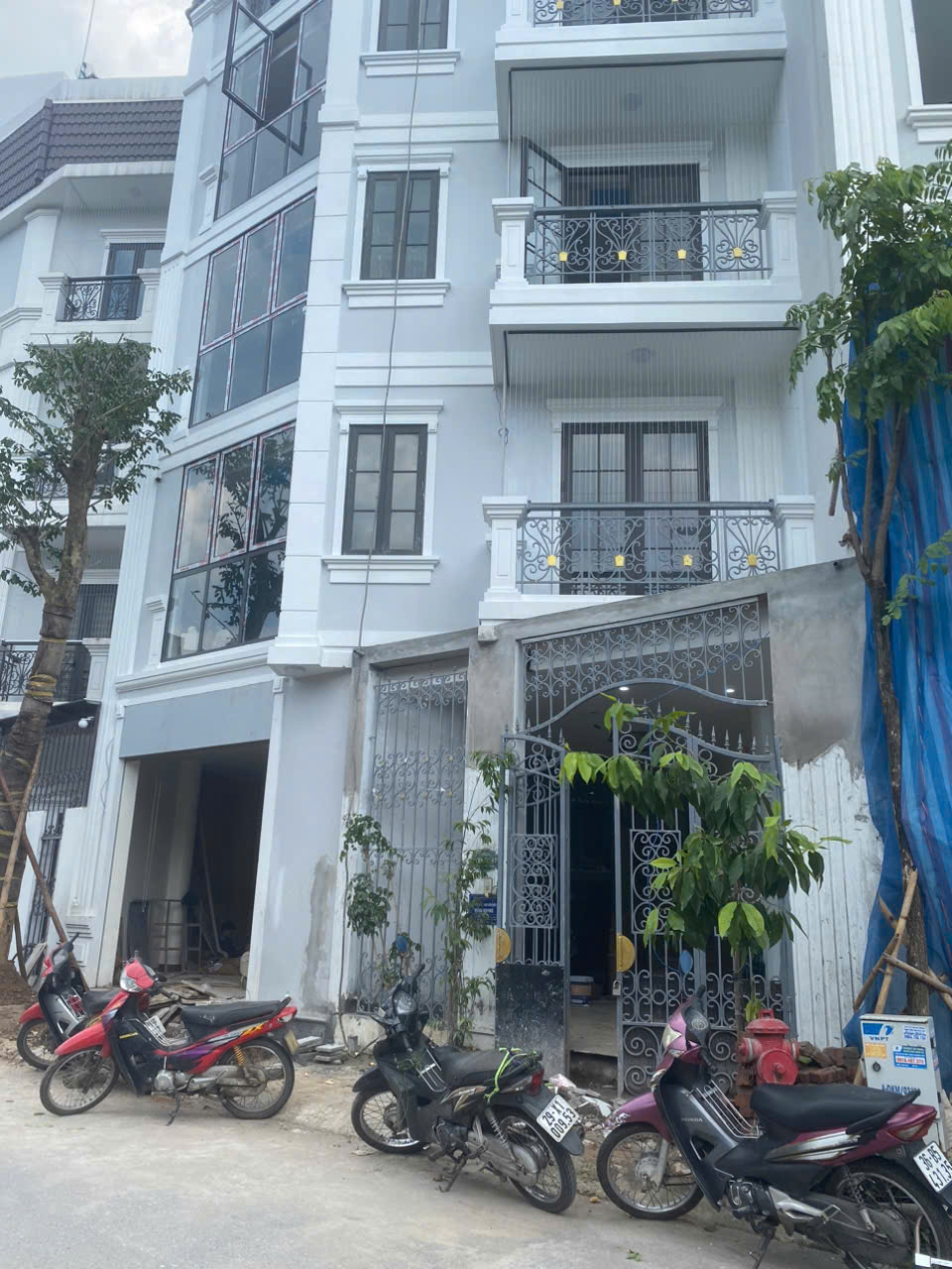 Mặt tiền nhà phố nhiều tầng đang hoàn thiện với cổng sắt và vài xe máy đỗ phía trước